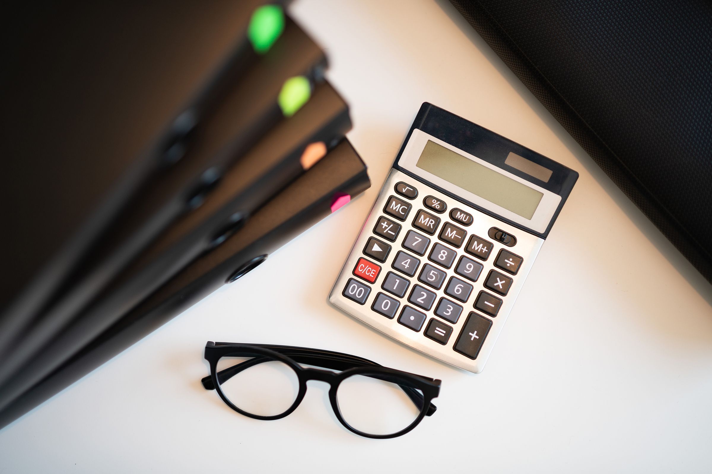 Calculadora, óculos e pastas sobre uma mesa de trabalho